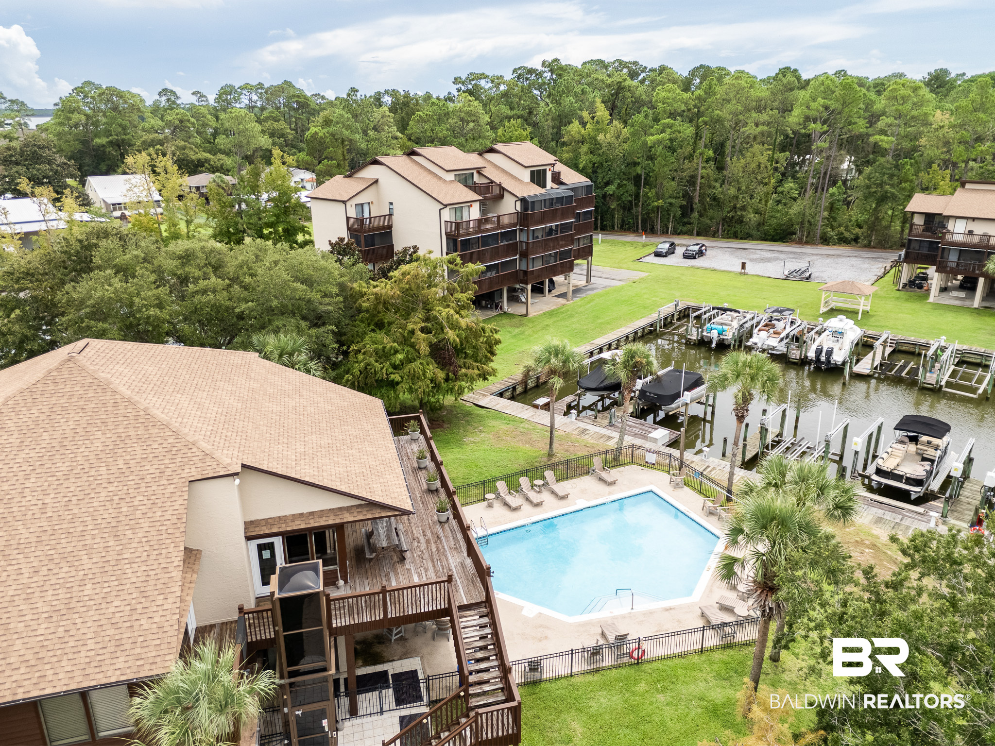 Aerial view of waterfront condominiums with a pool and marina docks lined with boats.