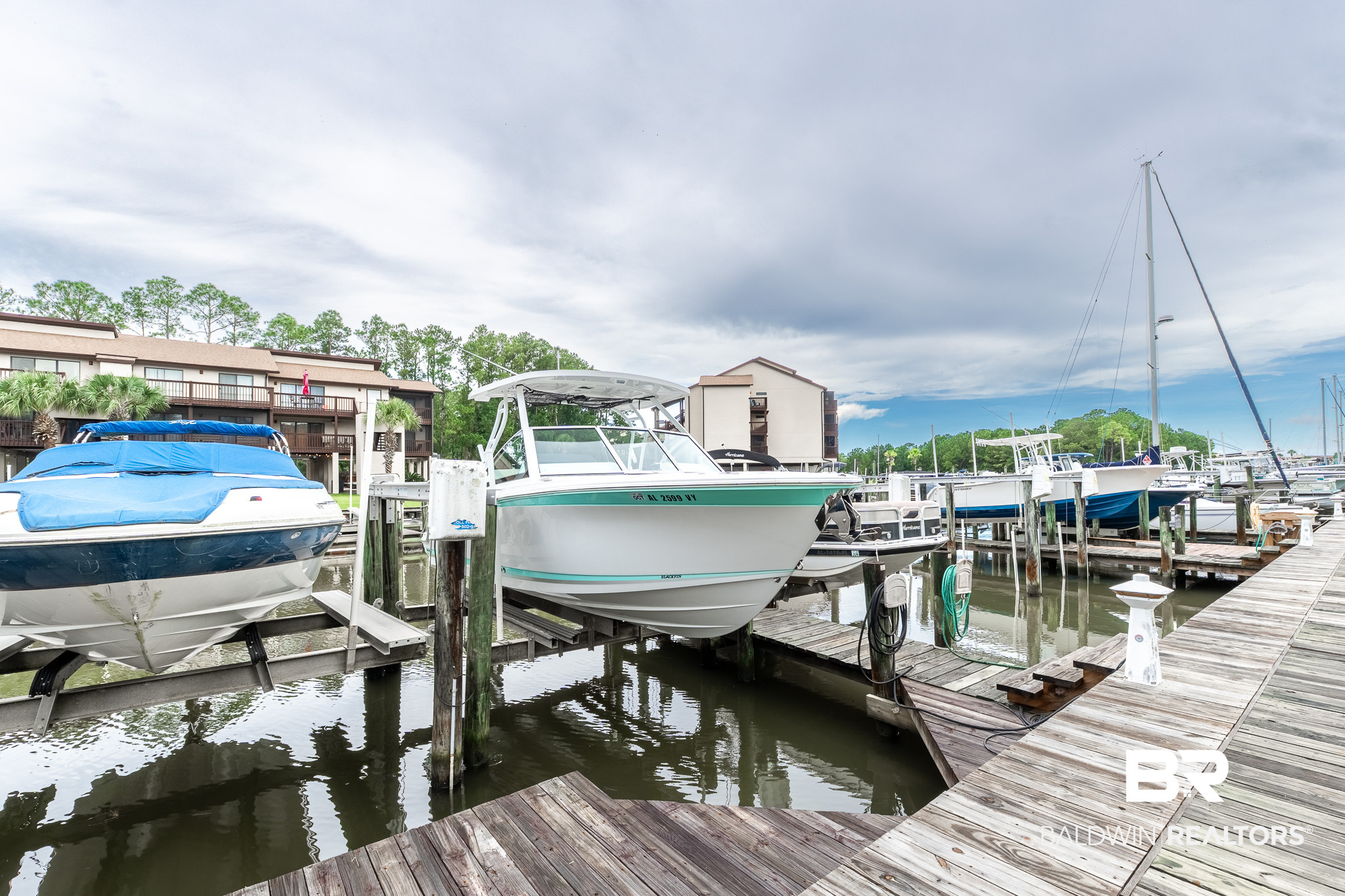 Boats moored at a marina dock, with waterfront condominium buildings behind them.