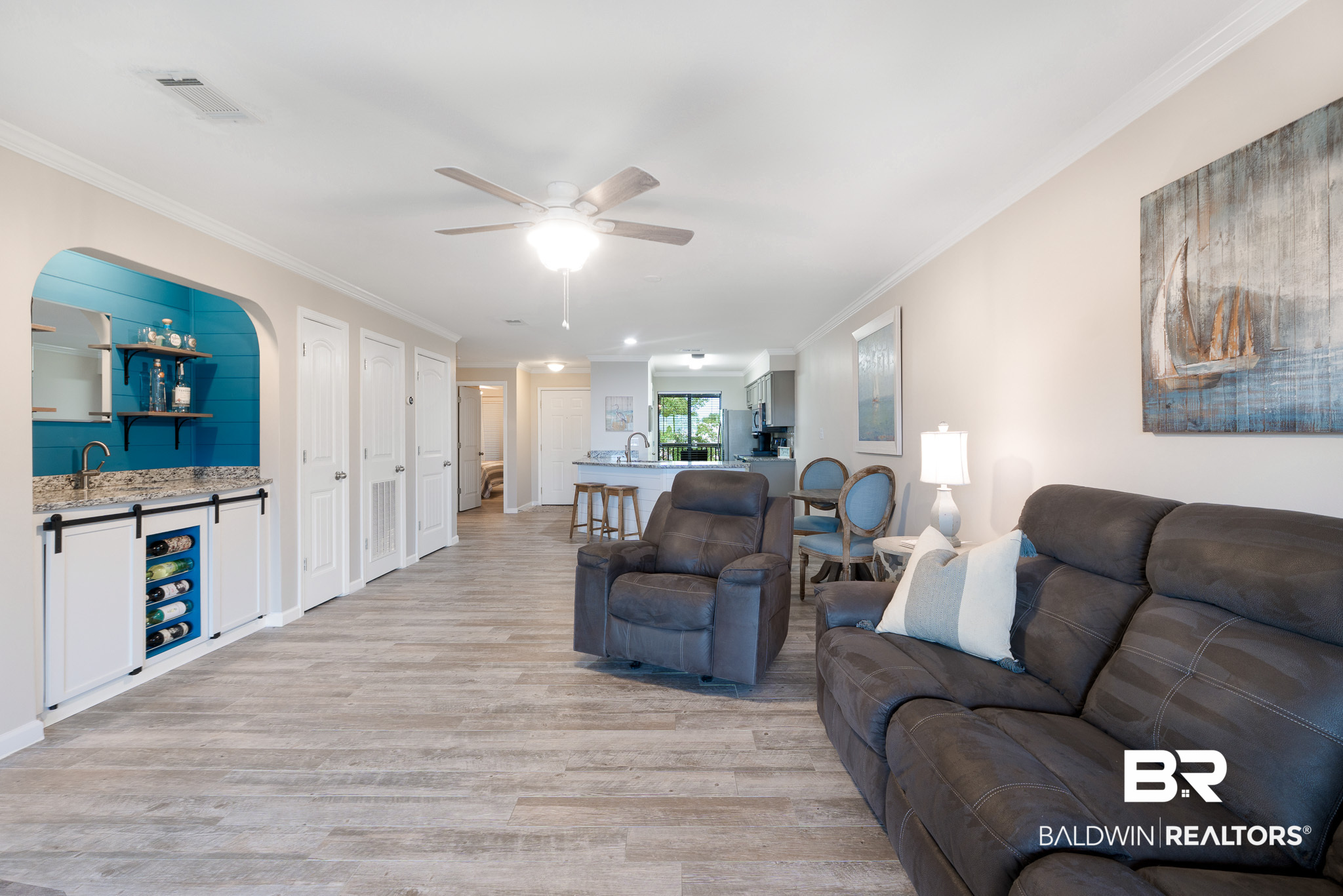 Open-plan condo living room with gray seating, a kitchen breakfast bar, and a bright blue built-in bar.