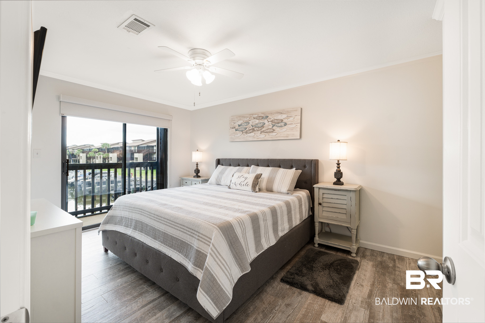 Furnished bedroom with a gray bed, matching nightstands, and sliding glass doors to a balcony.