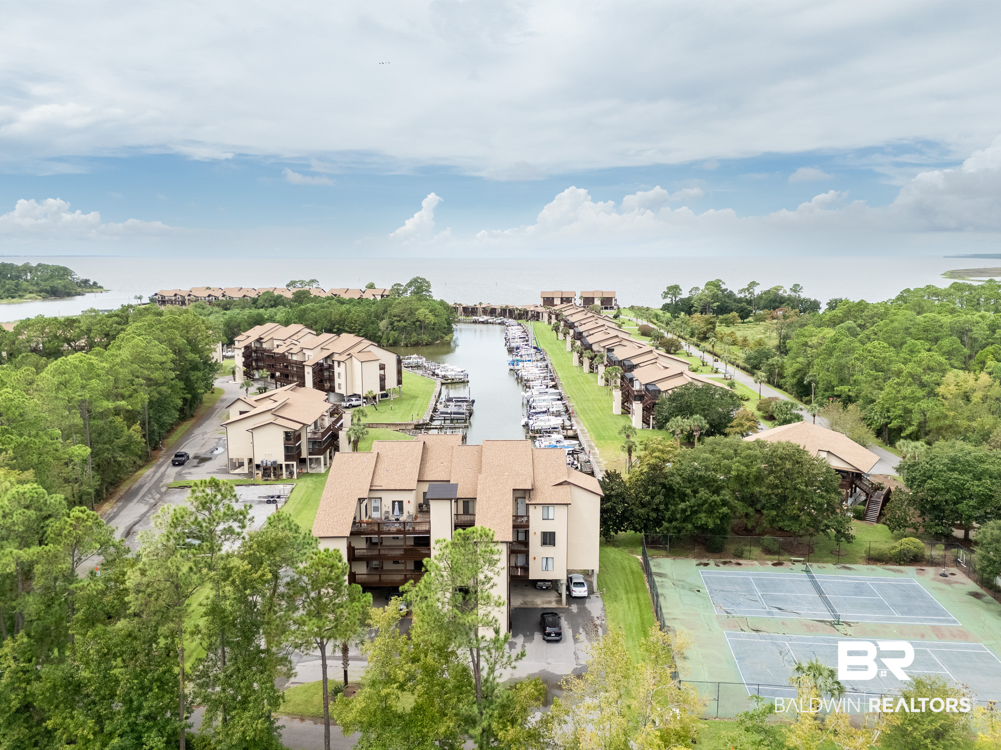 Aerial view of waterfront condominiums with a marina and tennis courts.