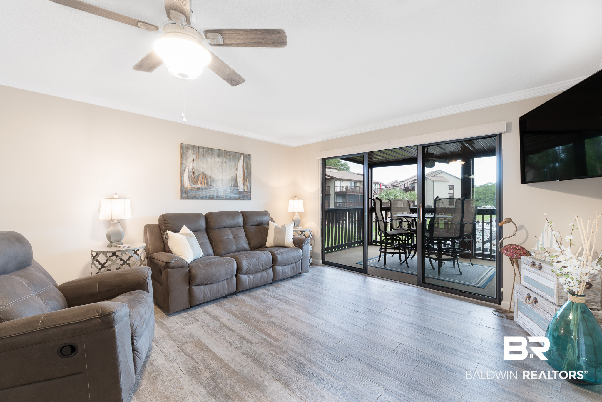 Furnished living room with reclining sofas and sliding doors opening to a covered balcony with patio seating.