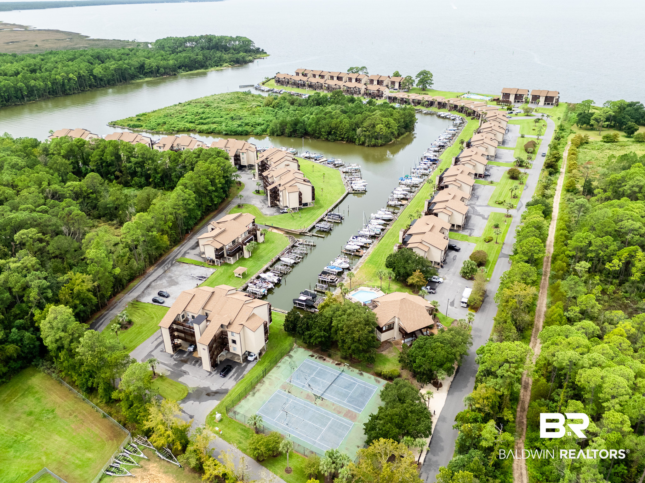 Waterfront condominium community with a marina, tennis courts, and pool, surrounded by wooded grounds.