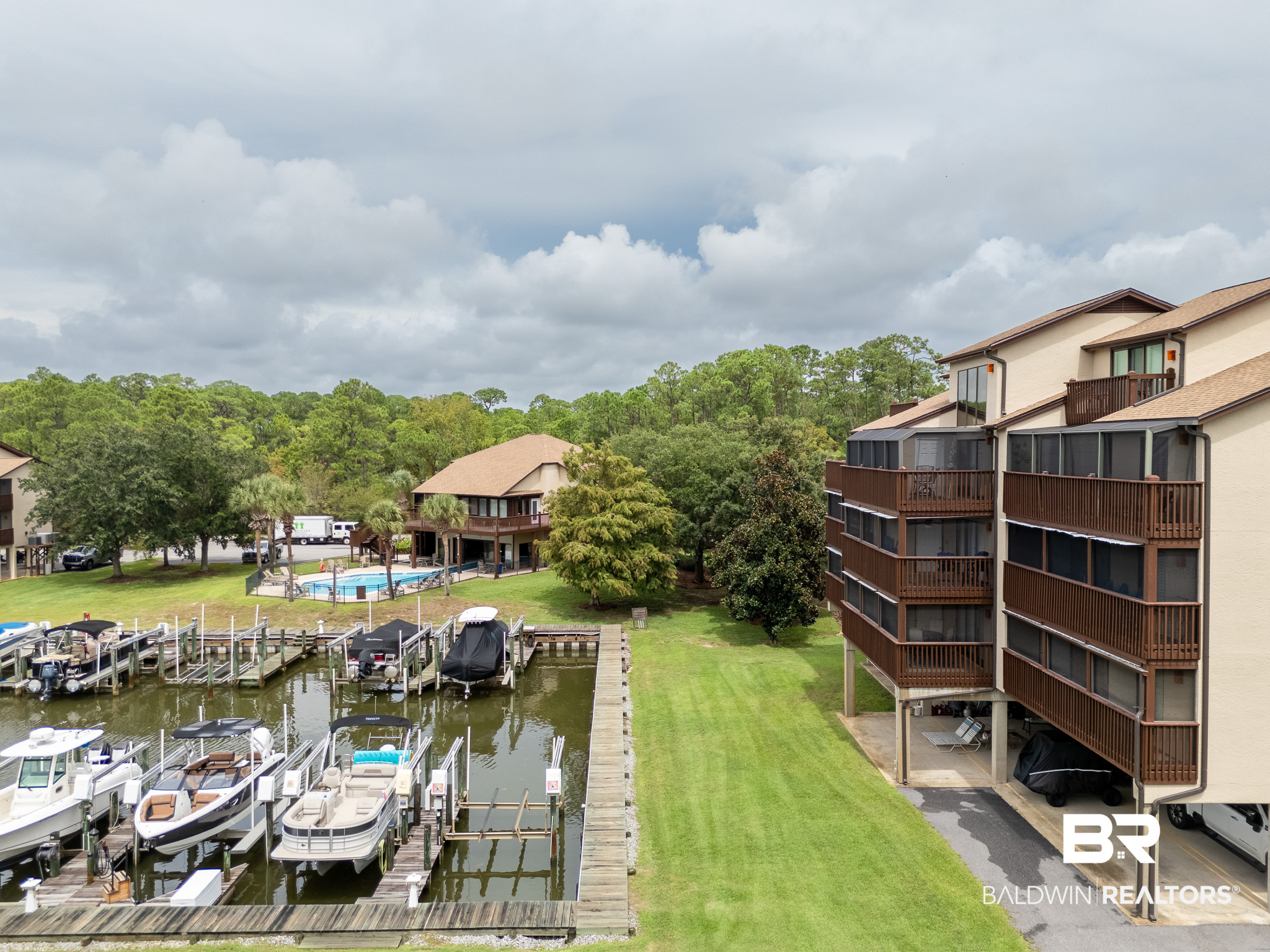 Waterfront condominium beside a marina, with boats, docks, a community pool, and a broad lawn.