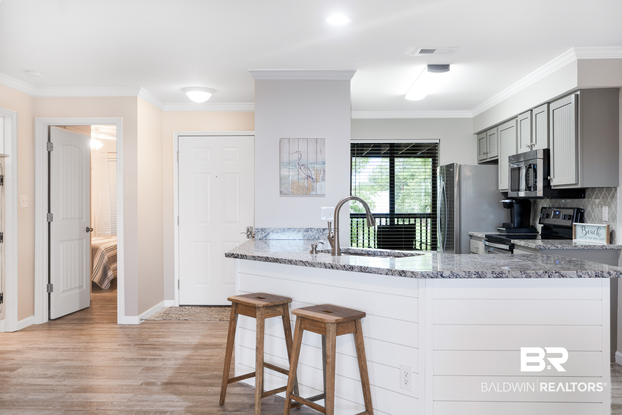 Condo kitchen with a granite island, two wooden stools, white cabinets, and stainless steel appliances.