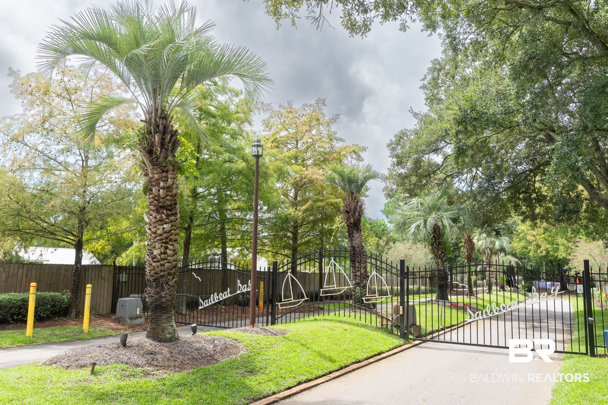 Sailboat Bay entrance with a decorative metal gate, palm trees, and landscaped grounds.