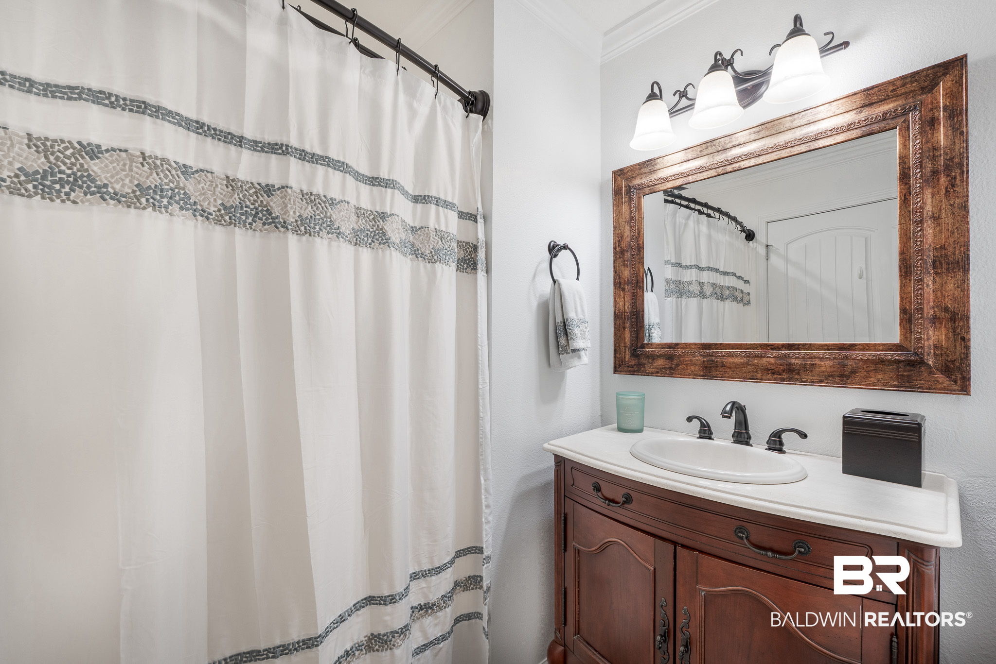 Bathroom vanity with dark wood cabinetry, a large framed mirror, and a patterned shower curtain.