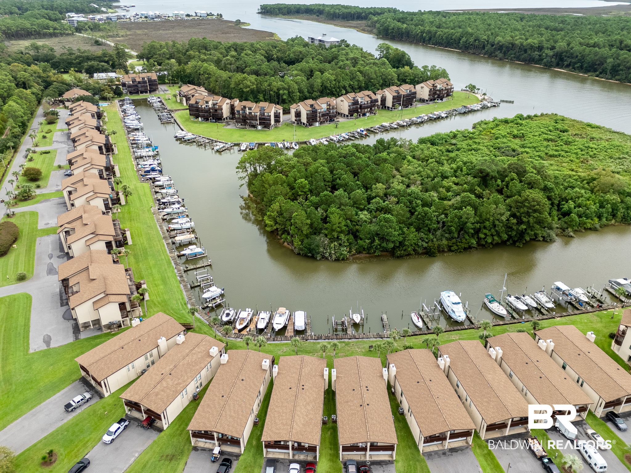 Aerial view of waterfront condos and a boat-filled marina beside a wooded island.