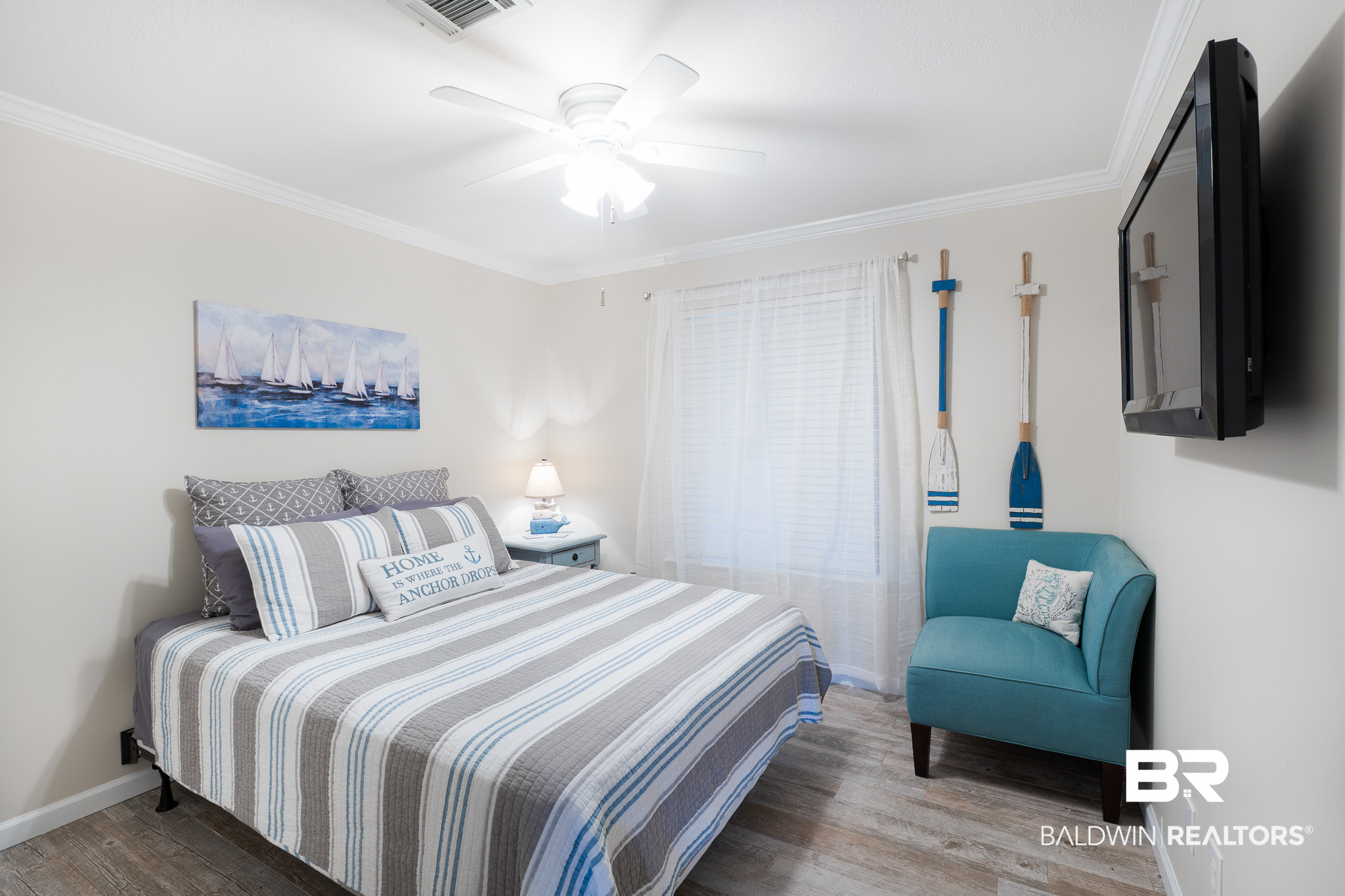 Bedroom with a striped bed, teal armchair, nautical decor, and wall-mounted television.