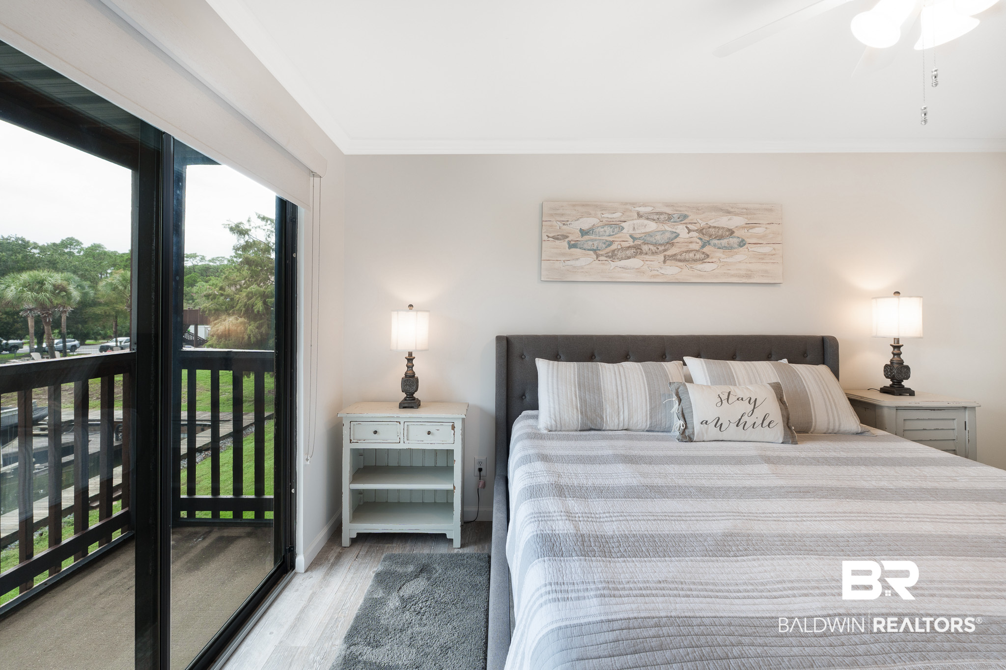 Bedroom with a gray upholstered bed and sliding doors opening onto a tree-lined balcony.