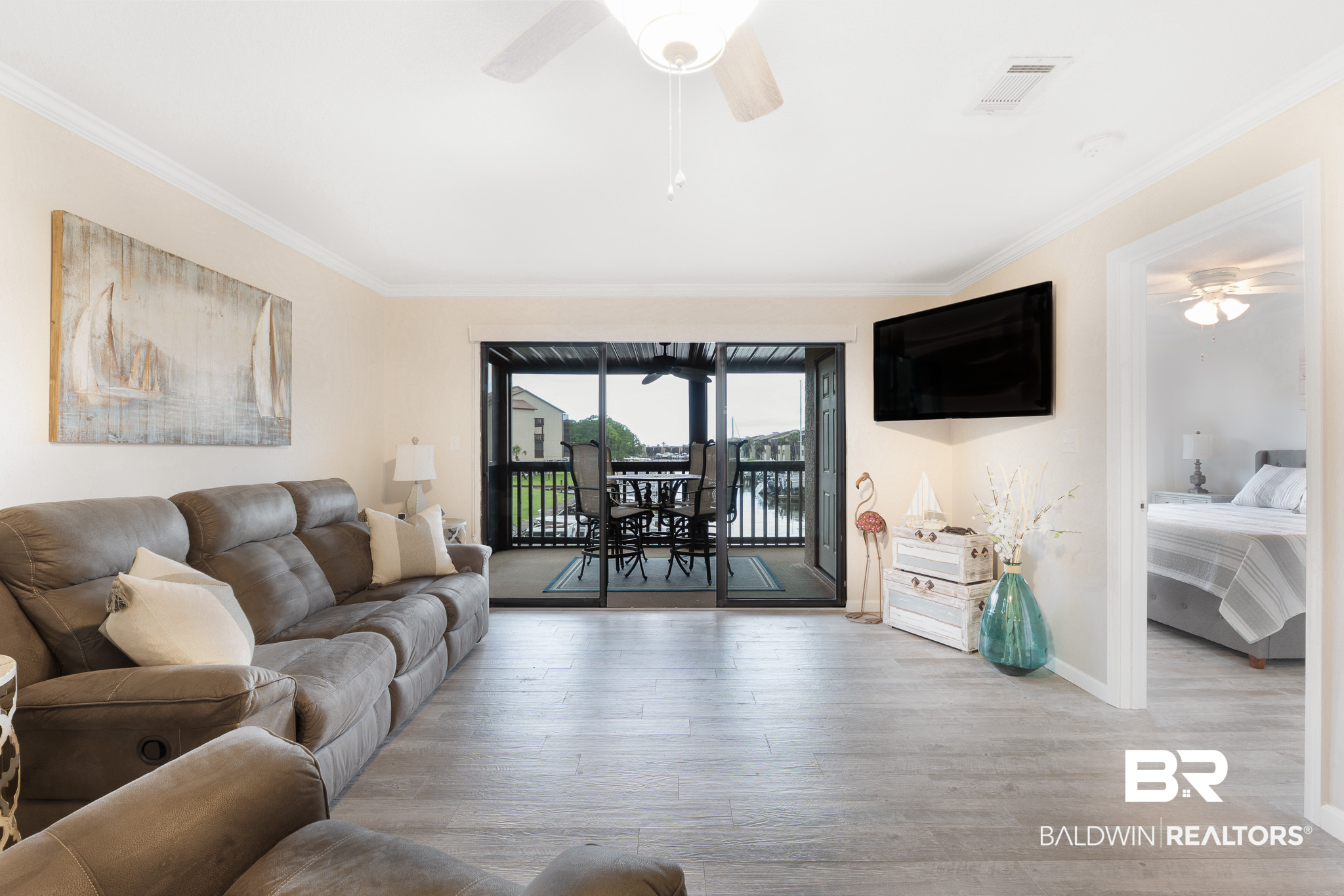 Living room with a gray sectional and sliding doors opening to a balcony overlooking the water.