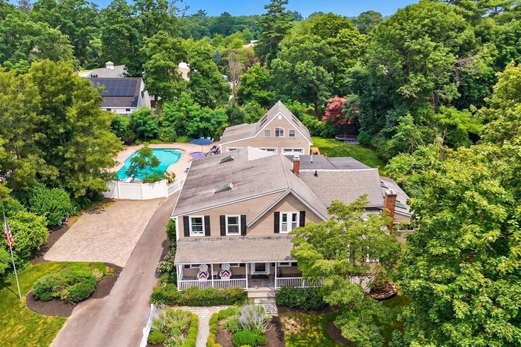 Aerial view of a tan house with a fenced swimming pool and tree-lined grounds.