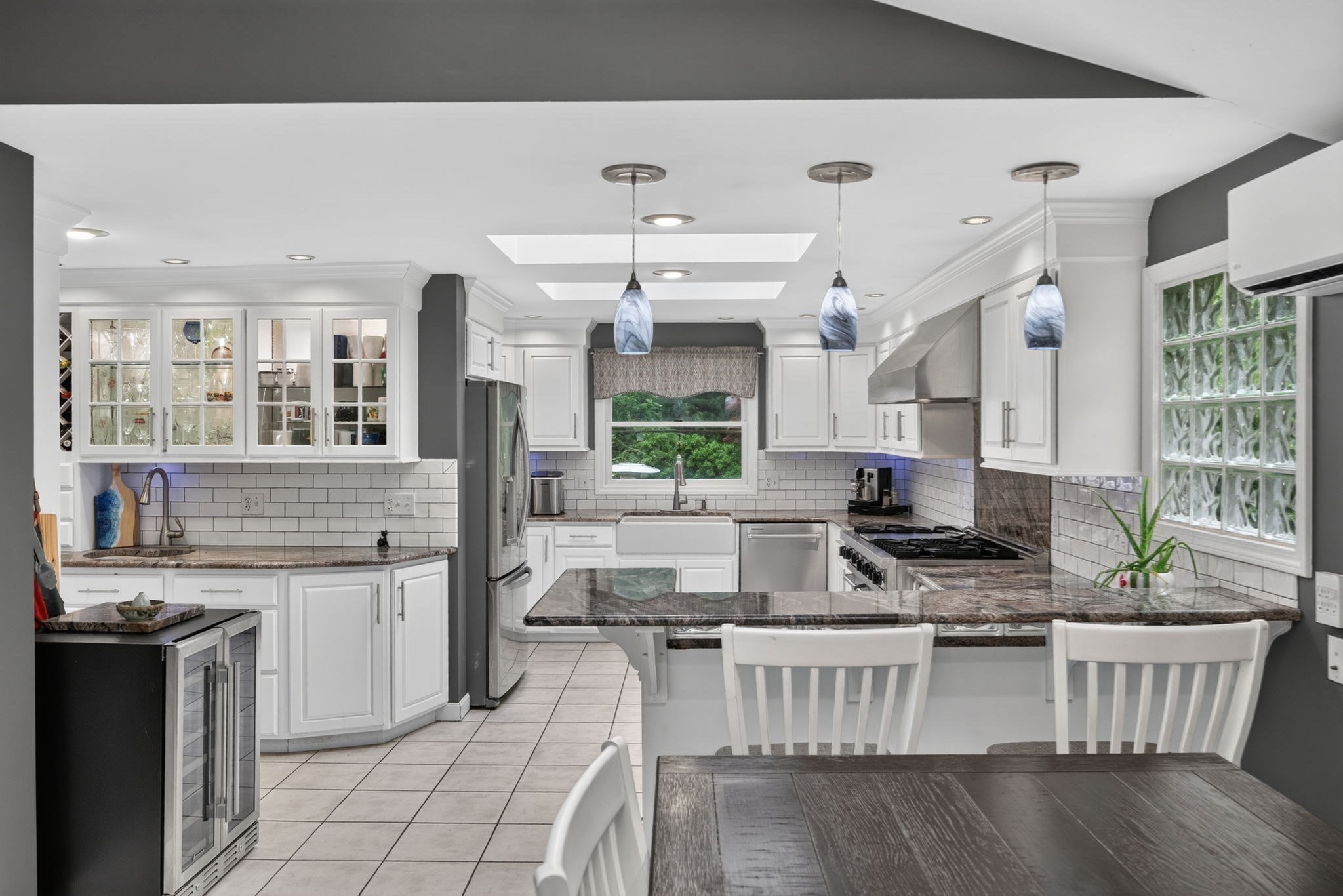 Bright white kitchen with a stone island, glass-front cabinets, and three pendant lights.