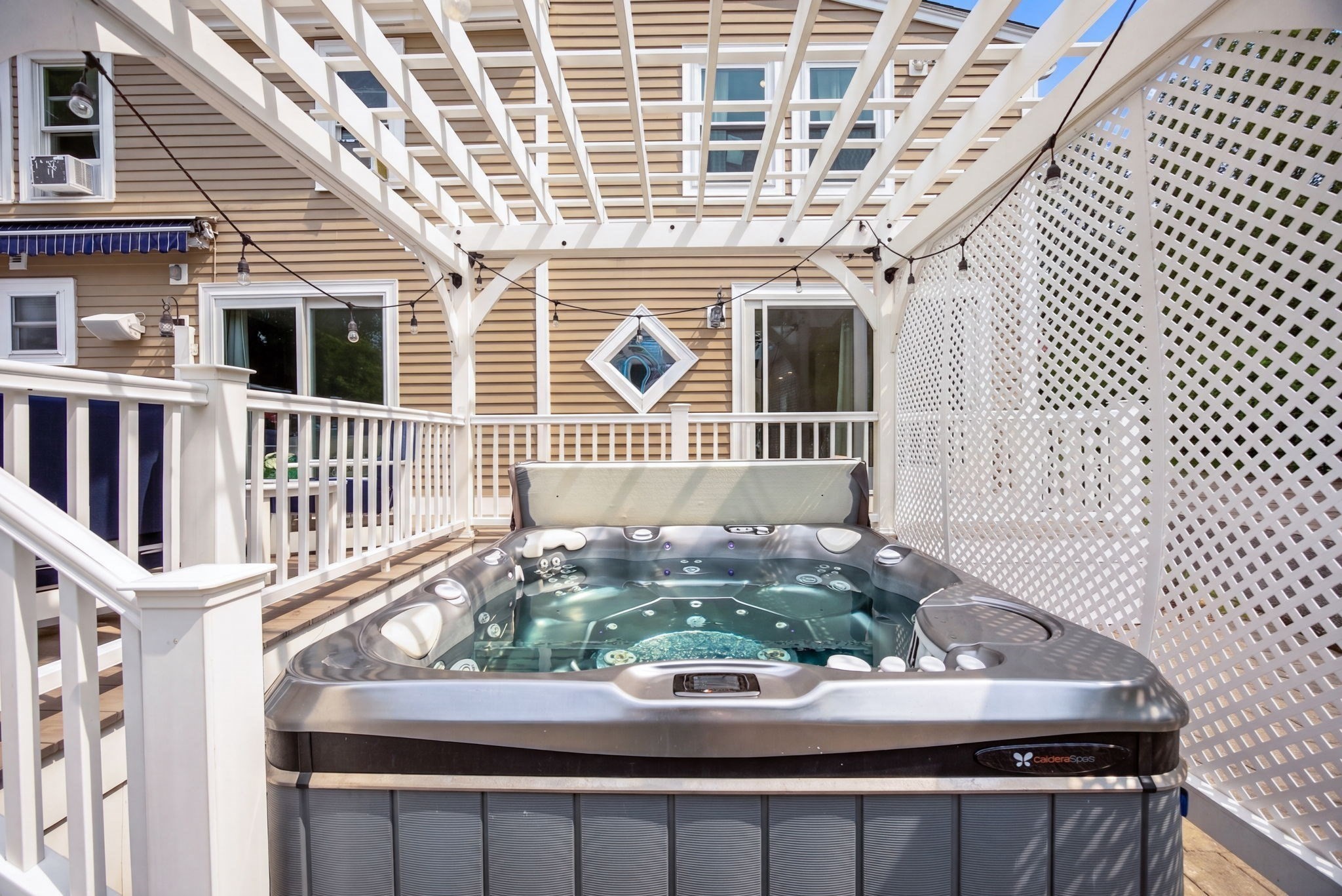 Outdoor hot tub beneath a white pergola on a deck with lattice privacy screening.