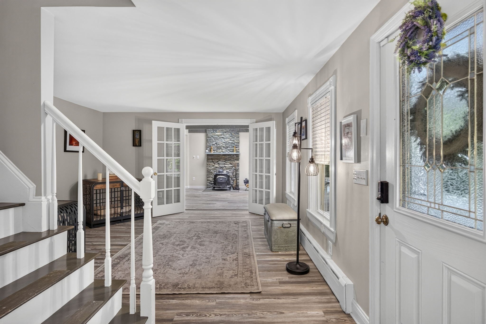 Entry hall with a stained-glass front door, staircase, and French doors opening toward a stone fireplace.