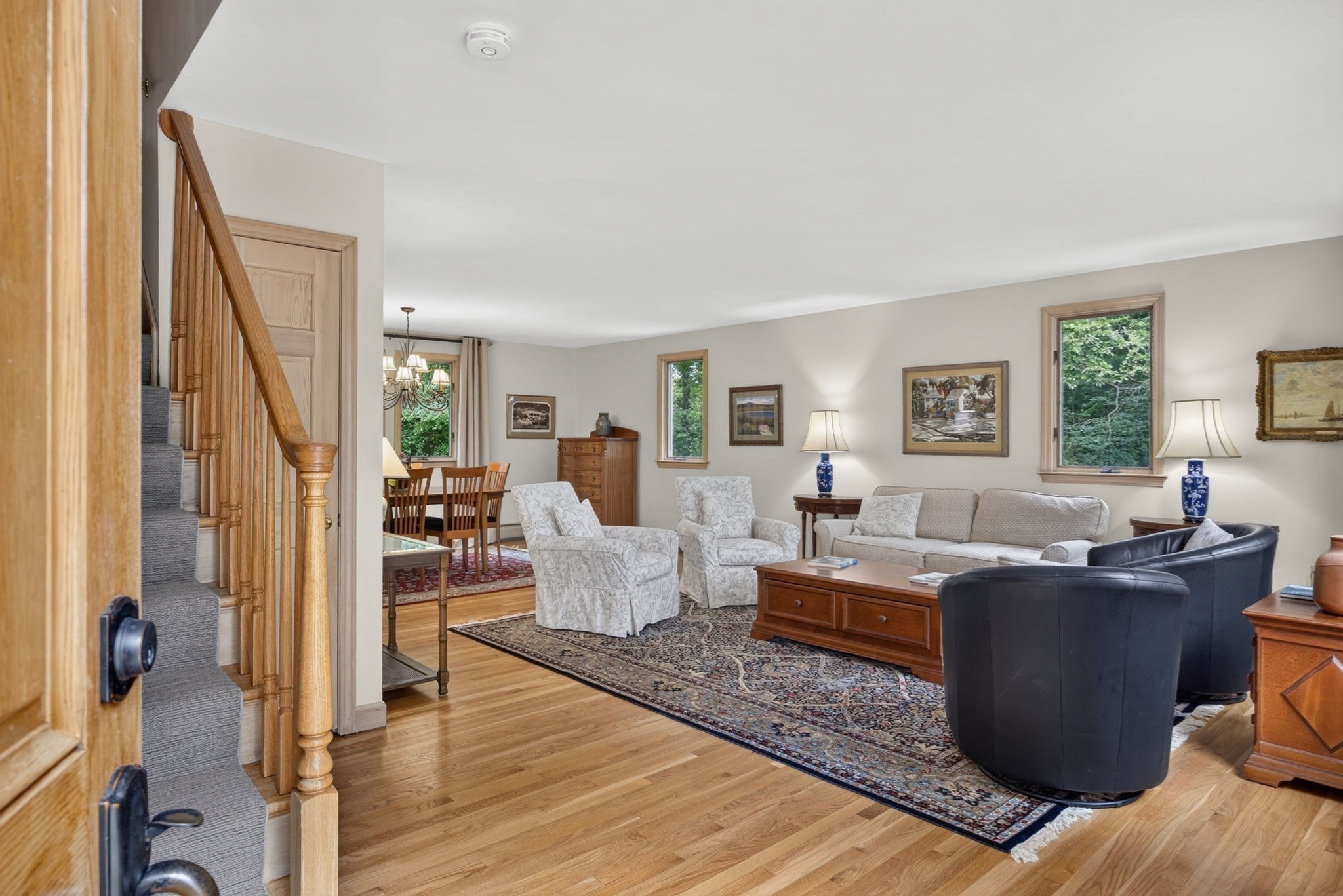Living room with hardwood floors, patterned rug, and a wooden staircase beside the seating area.