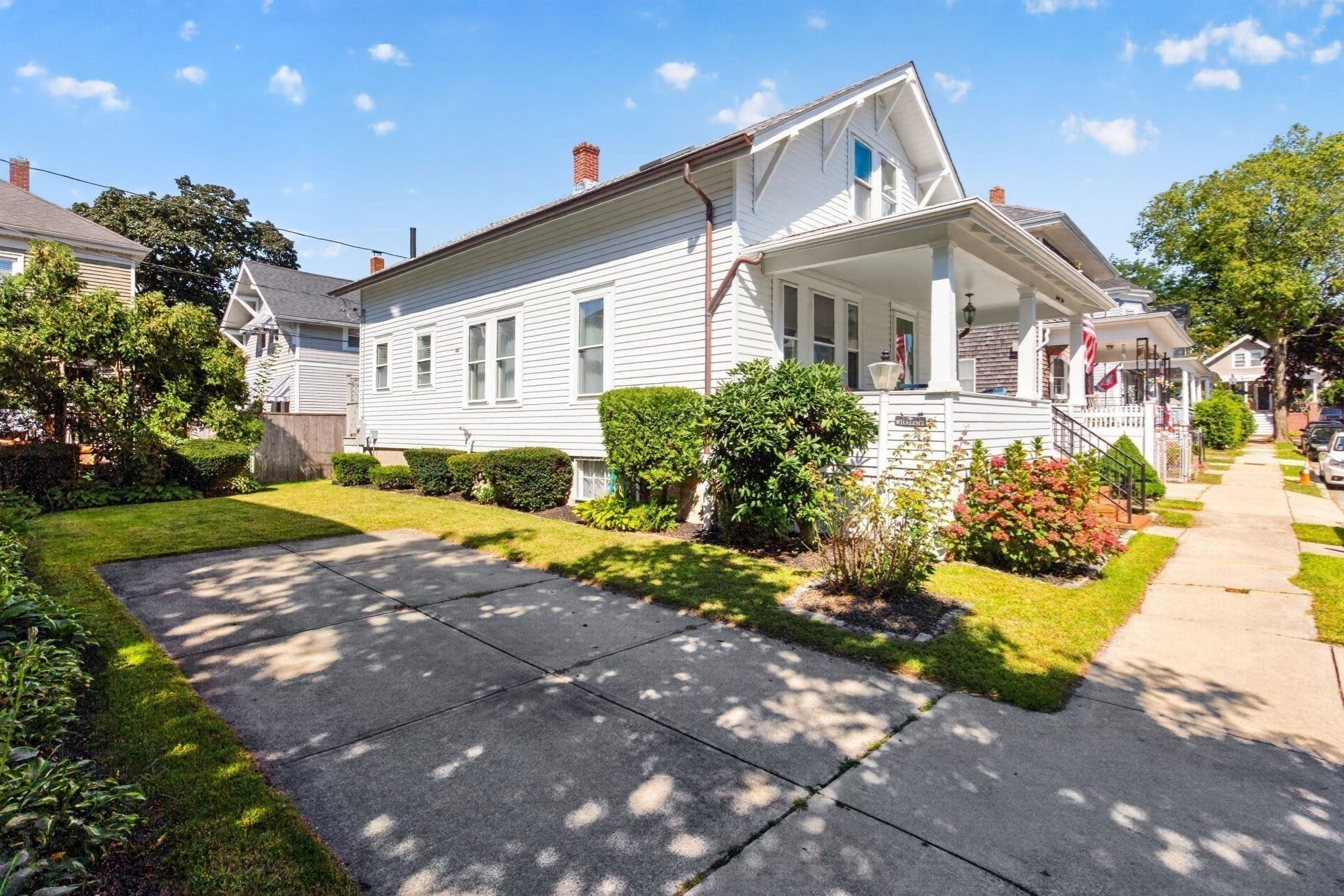 White two-story house with a covered porch, landscaped front yard, and broad concrete walkway.