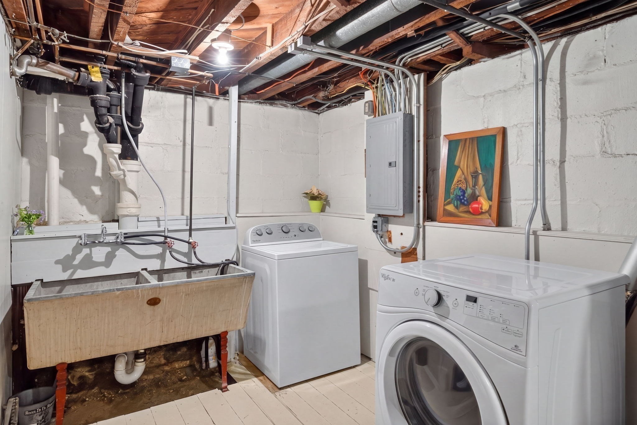Basement laundry room with a utility sink, washer, dryer, exposed joists, and electrical panel.