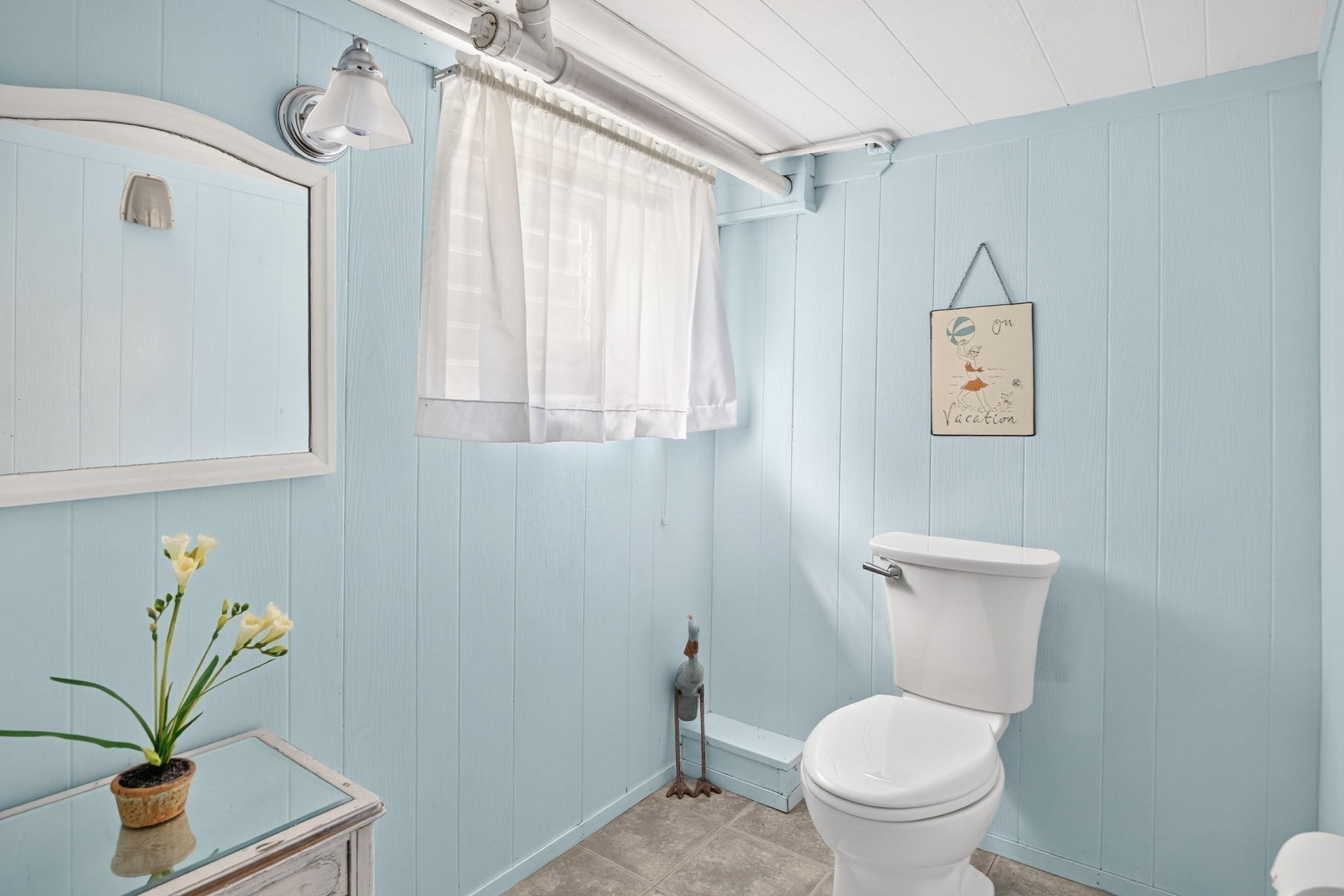 Bathroom with pale blue paneled walls, a white toilet, and a curtained window.