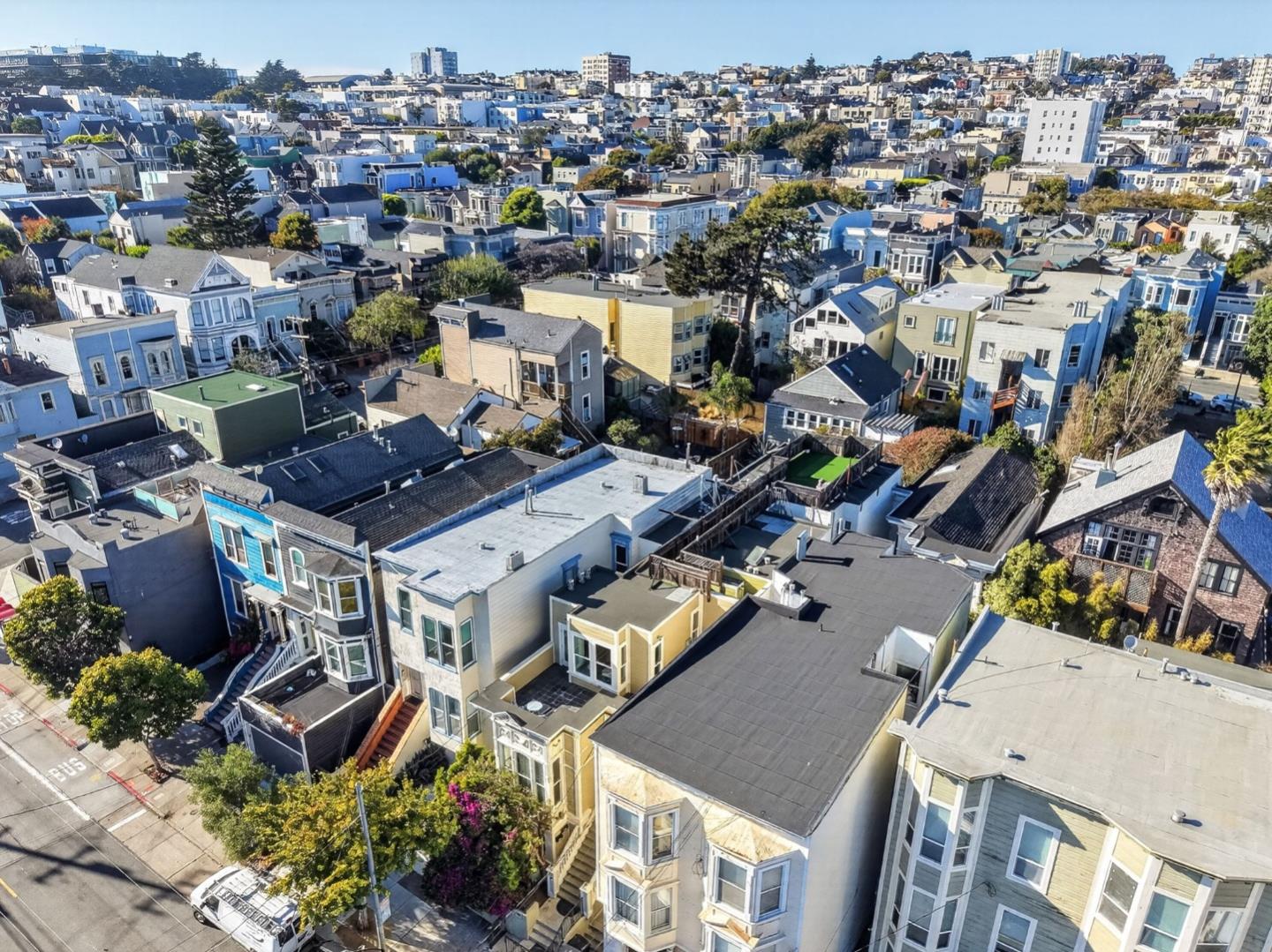 Aerial view over dense San Francisco residential blocks with varied rooftops and bay-windowed homes.