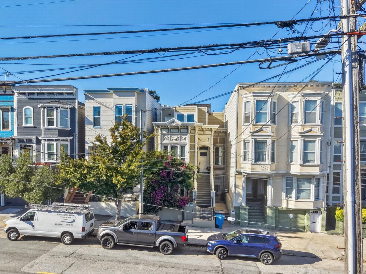 Ornate tan Victorian home between bay-window houses, seen across a San Francisco street.