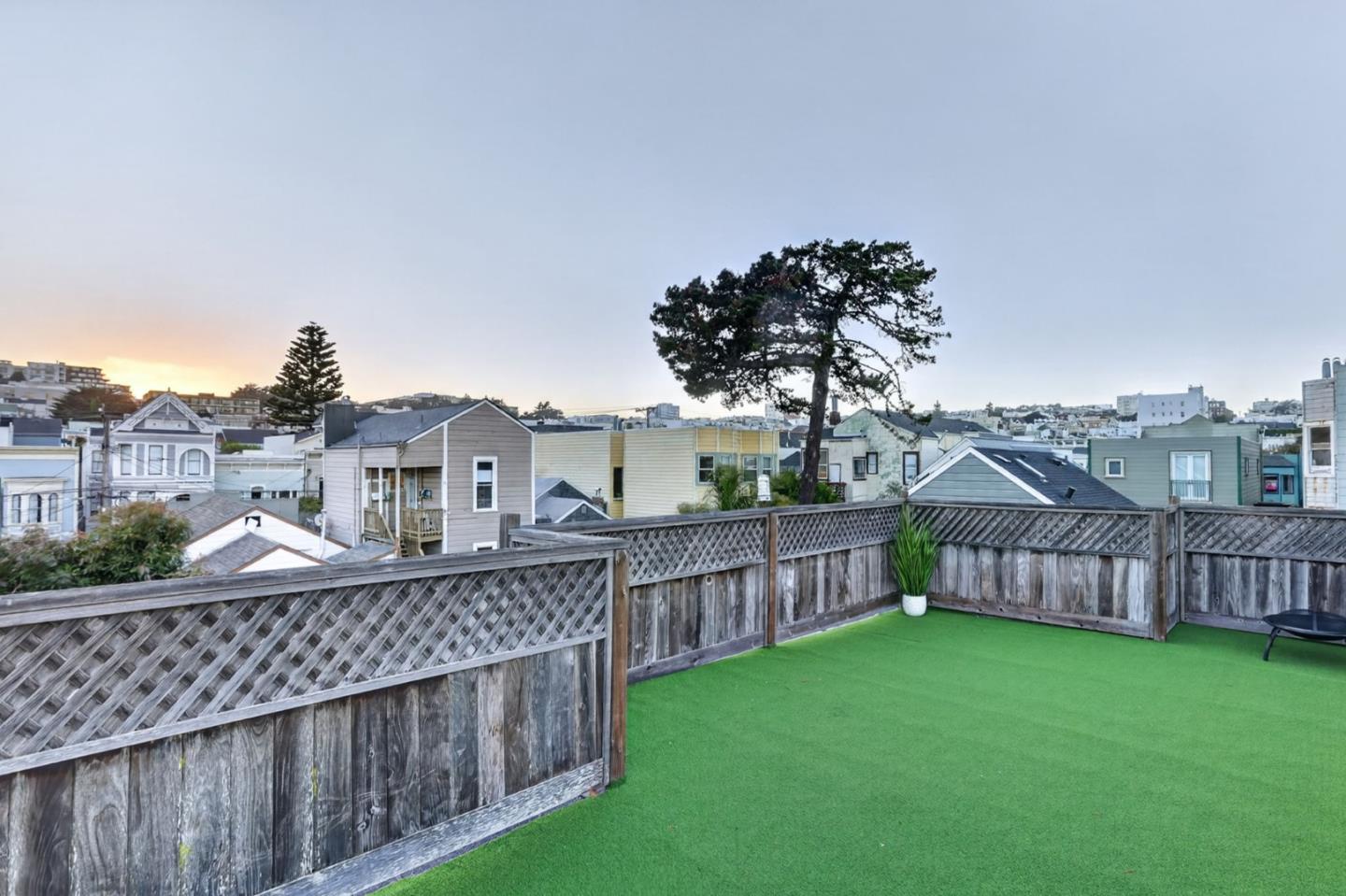 Rooftop deck with green turf and lattice fencing overlooking neighboring rooftops at dusk.