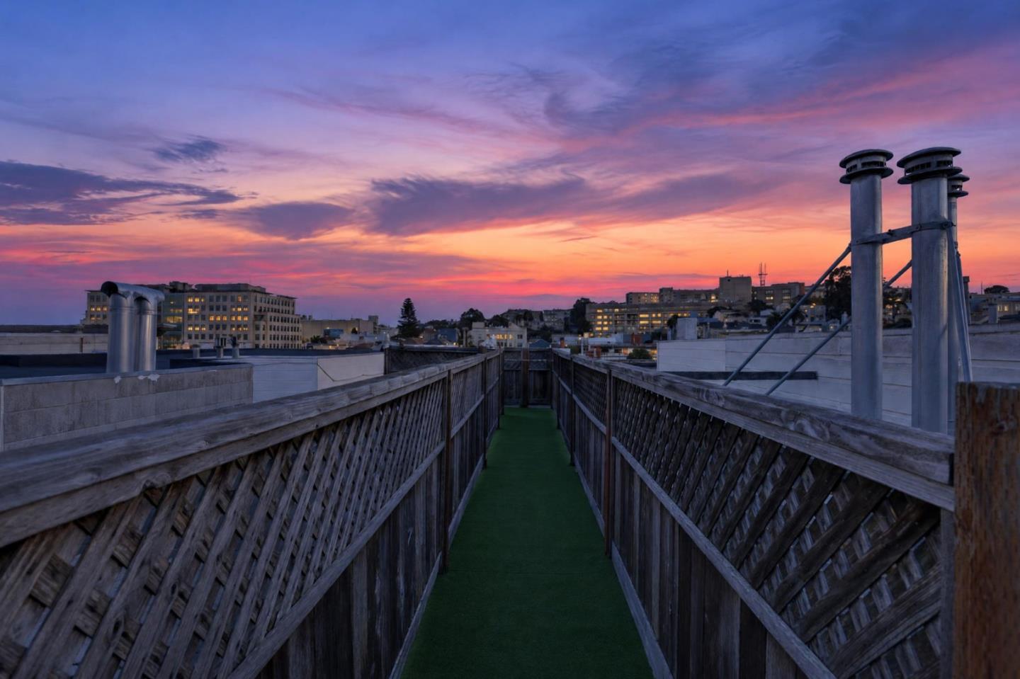 Rooftop walkway with wooden railings and city skyline beneath a colorful dusk sky.