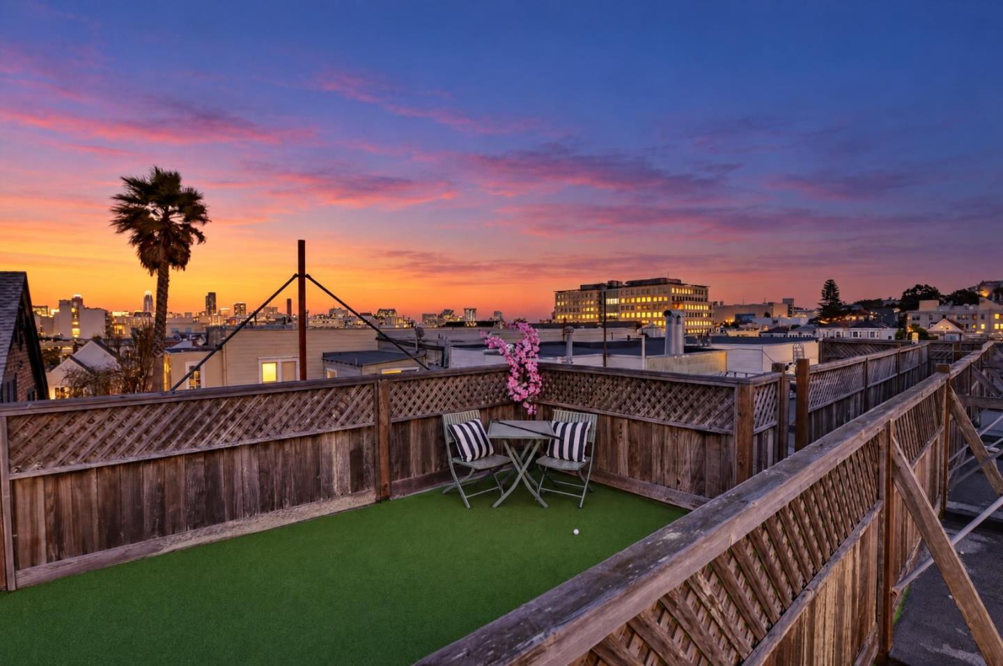 Rooftop deck with artificial turf and café seating overlooking the skyline at sunset.
