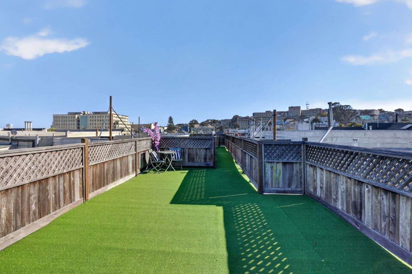 Rooftop deck with green turf, wooden lattice fencing, folding chairs, and city views.