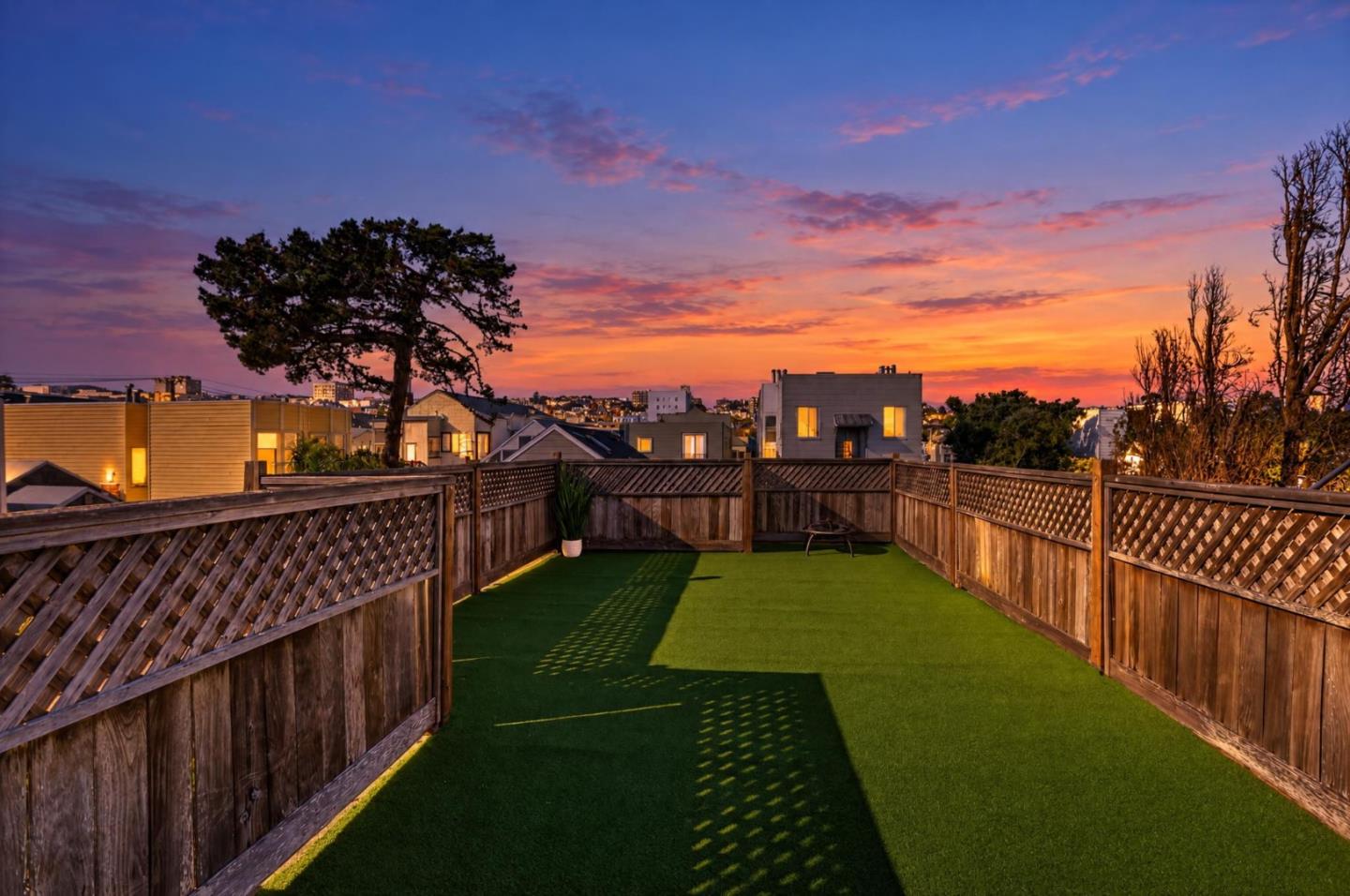 Rooftop deck with artificial turf and wooden fencing overlooking San Francisco homes at sunset.