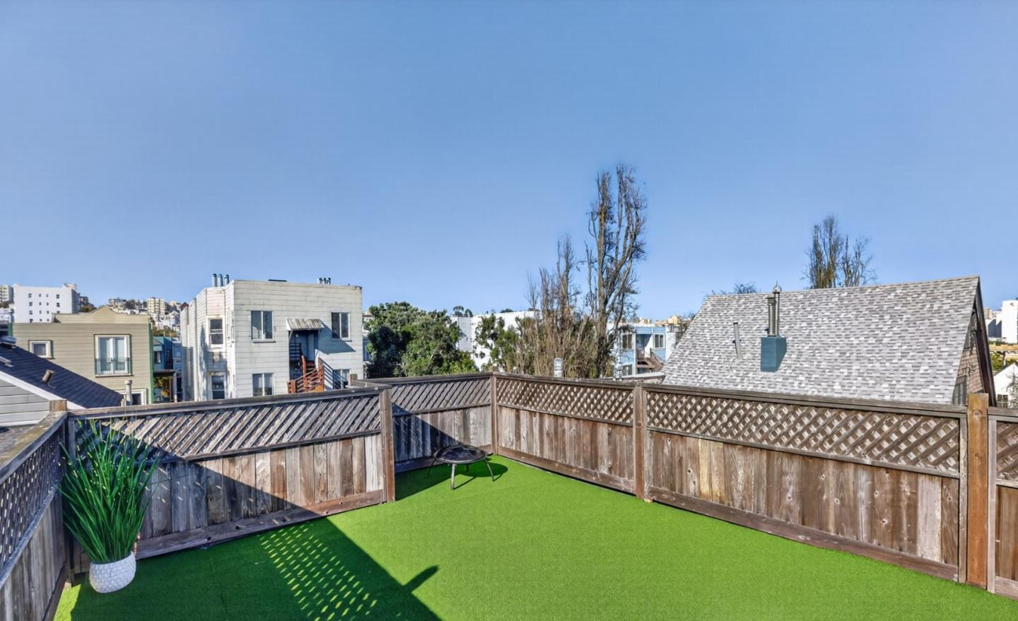 Rooftop deck with green turf and wooden lattice fencing, overlooking neighboring buildings.