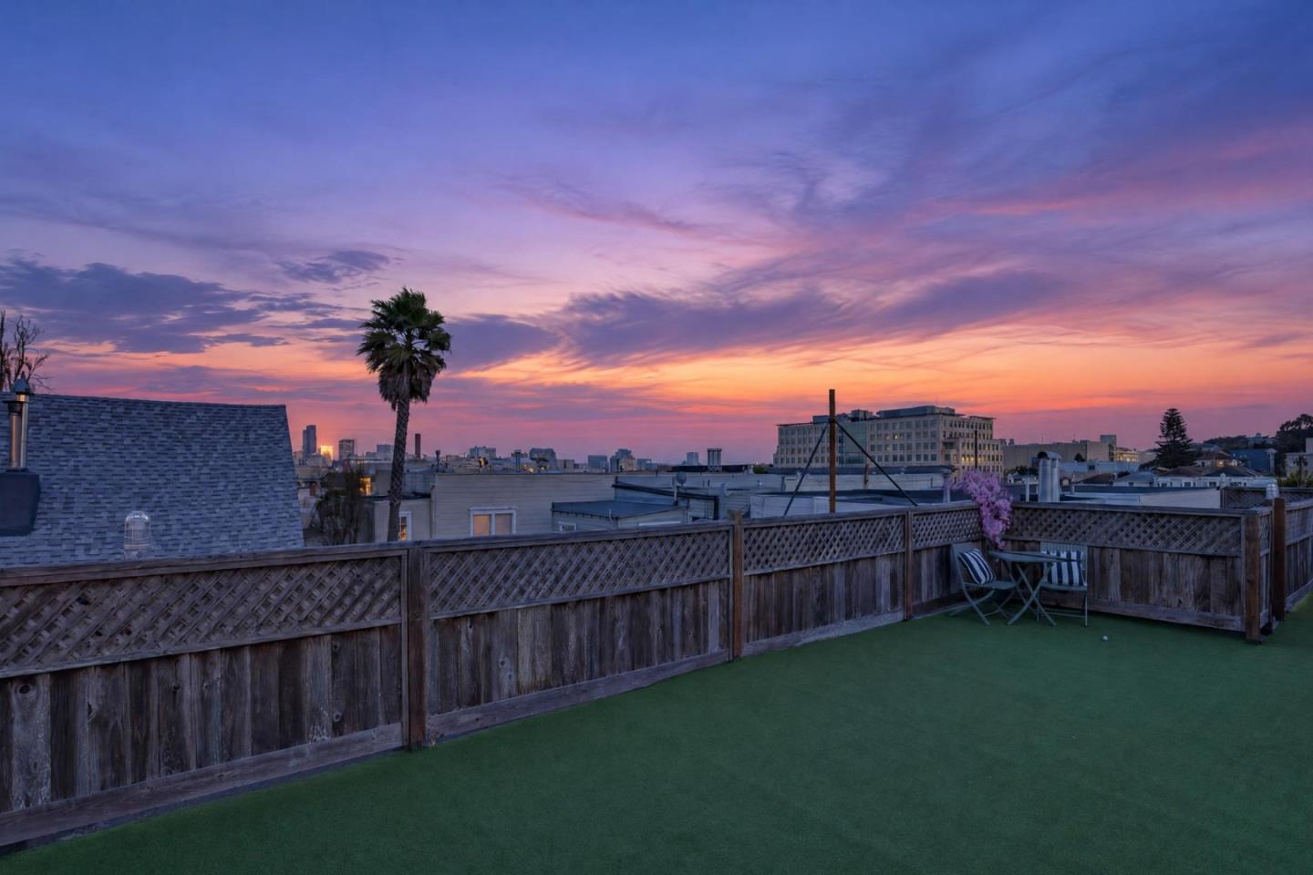 Rooftop deck with turf and outdoor seating overlooking city rooftops at dusk.