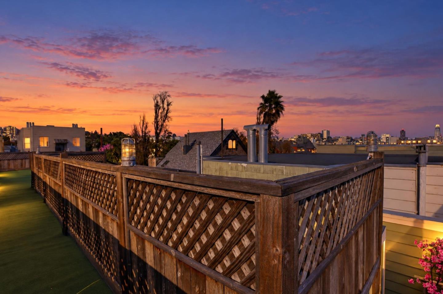Rooftop deck with artificial turf and a wooden lattice fence overlooking the San Francisco skyline at sunset.
