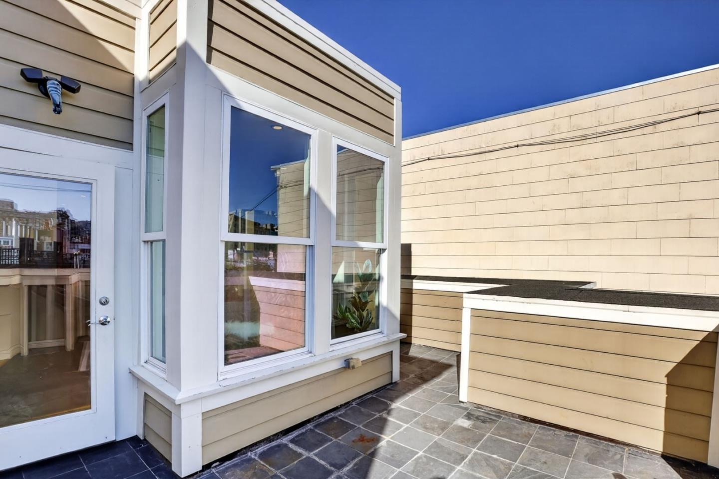 Rooftop terrace with dark tiled flooring, beige privacy walls, and white-framed windows.