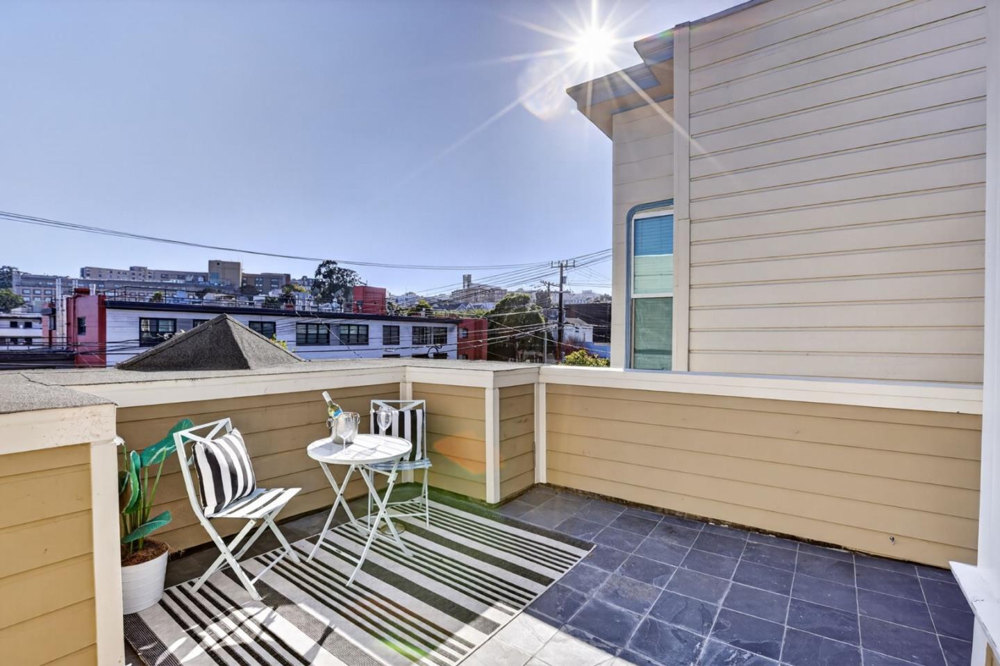 Rooftop terrace with striped outdoor rug, seating, and views of nearby buildings.