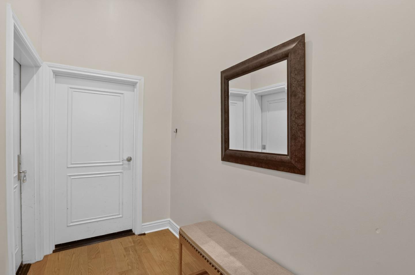 Hallway with white paneled doors, a dark-framed mirror, and a narrow upholstered bench.