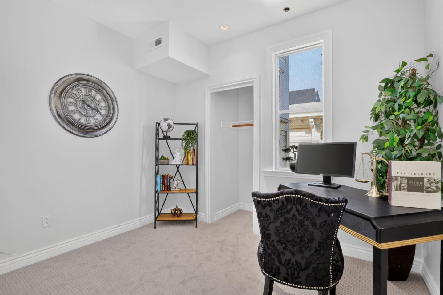Staged home office with a black desk, patterned chair, tall window, and bookshelf.