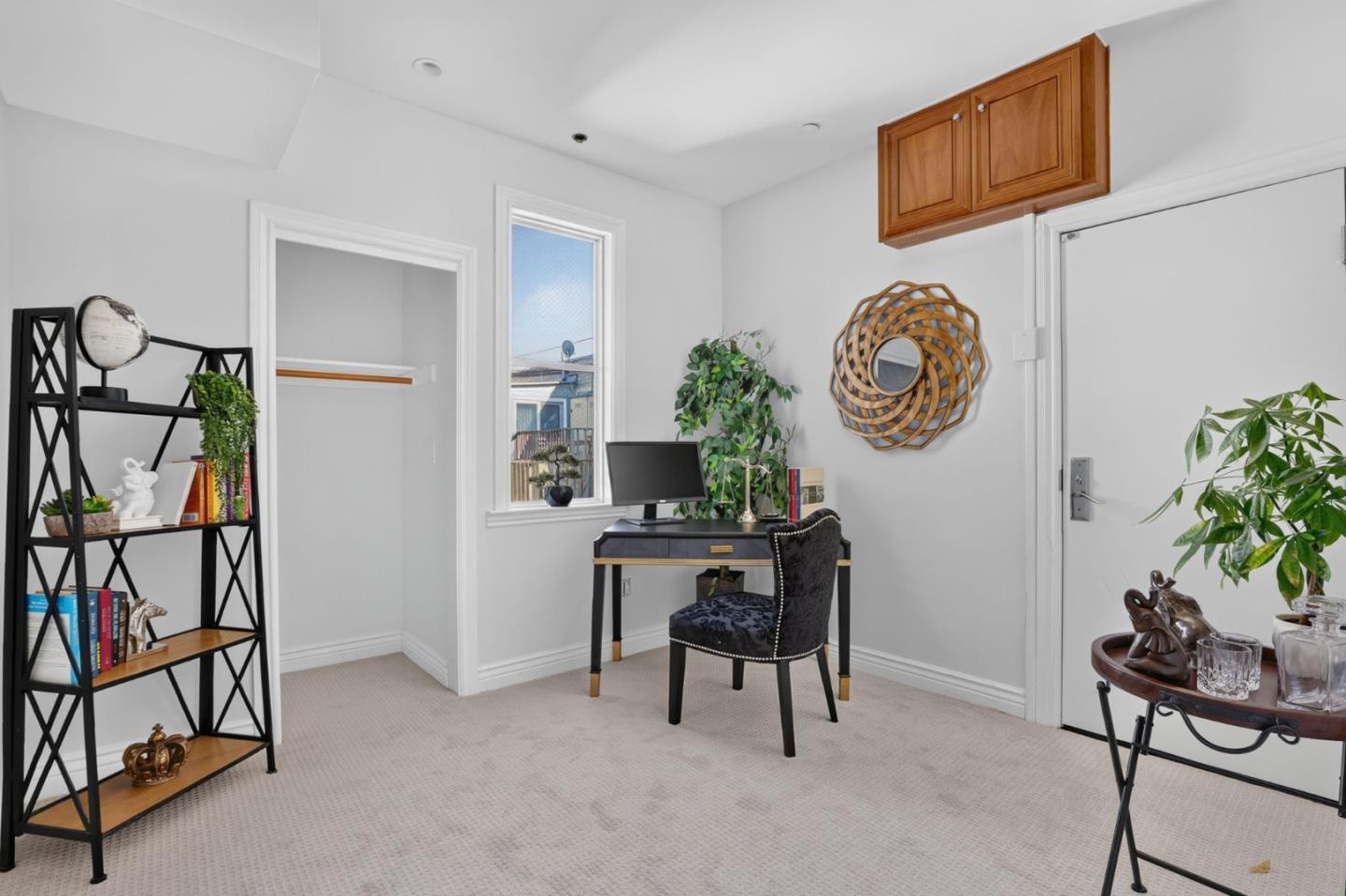 Furnished home office with a black desk beneath a window and a tall bookshelf.