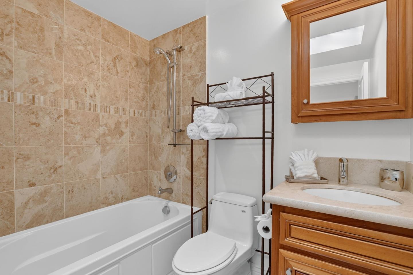 Bathroom with a tiled tub and shower, wood vanity, framed mirror, and neatly folded towels.