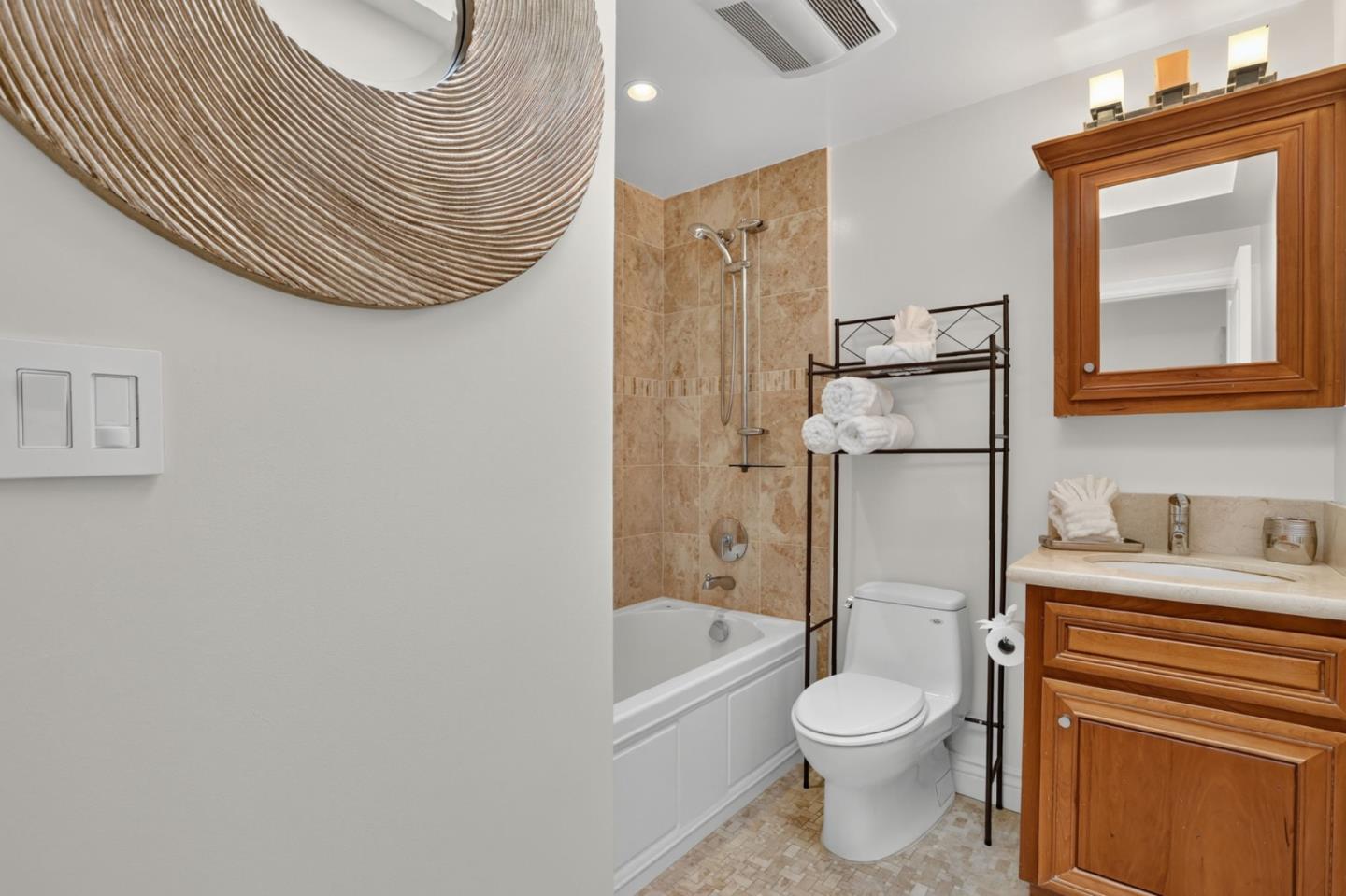 Bathroom with a tan-tile tub and shower, wood vanity, and towel rack.
