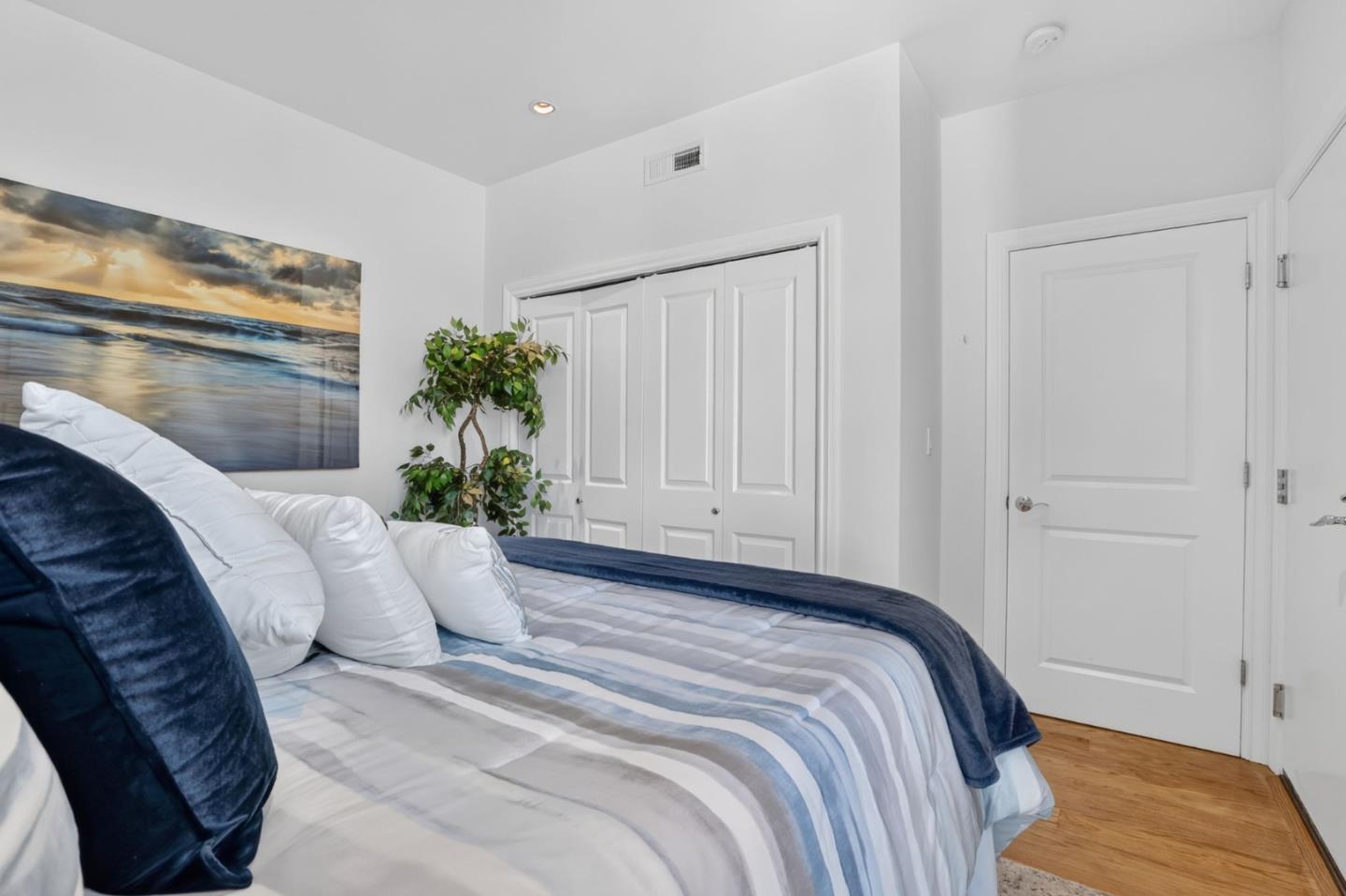 Bedroom with striped bedding, navy pillows, a potted plant, and white closet doors.