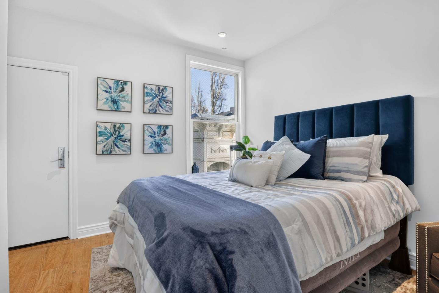 Staged bedroom with a navy headboard, blue throw, and four abstract prints beside the window.