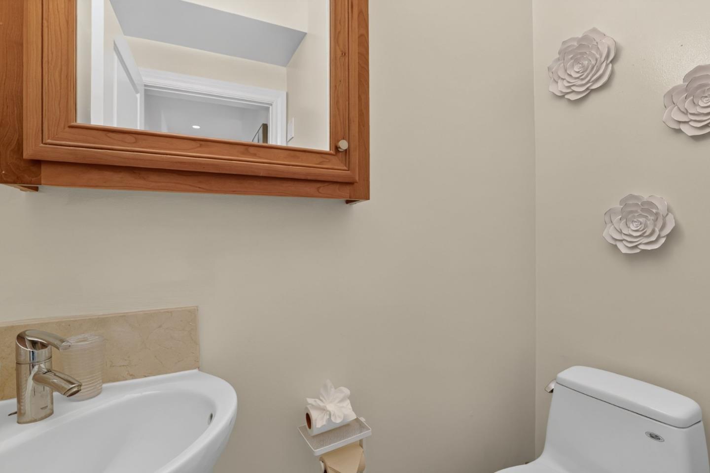 Bathroom with a wood-framed mirrored cabinet, white sink and toilet, and flower wall decorations.