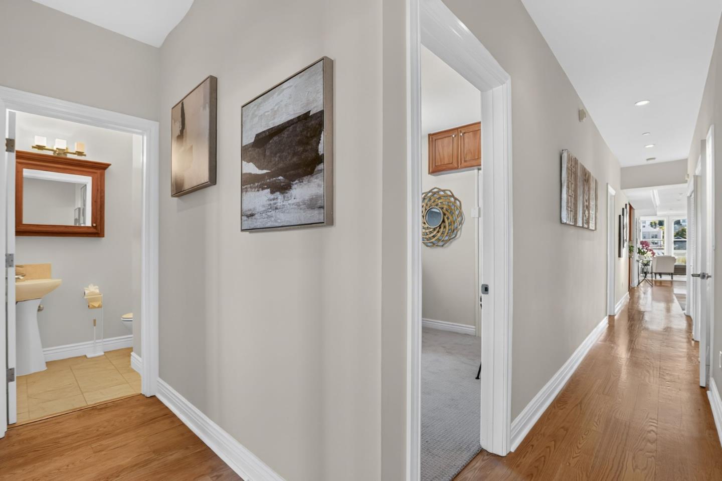 Hallway with polished hardwood floors, framed artwork, and open doorways to adjacent rooms.