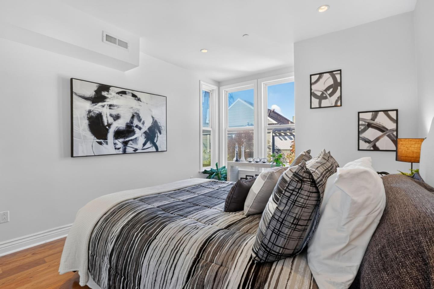 Staged bedroom with a large striped bed, layered pillows, abstract artwork, and tall windows.