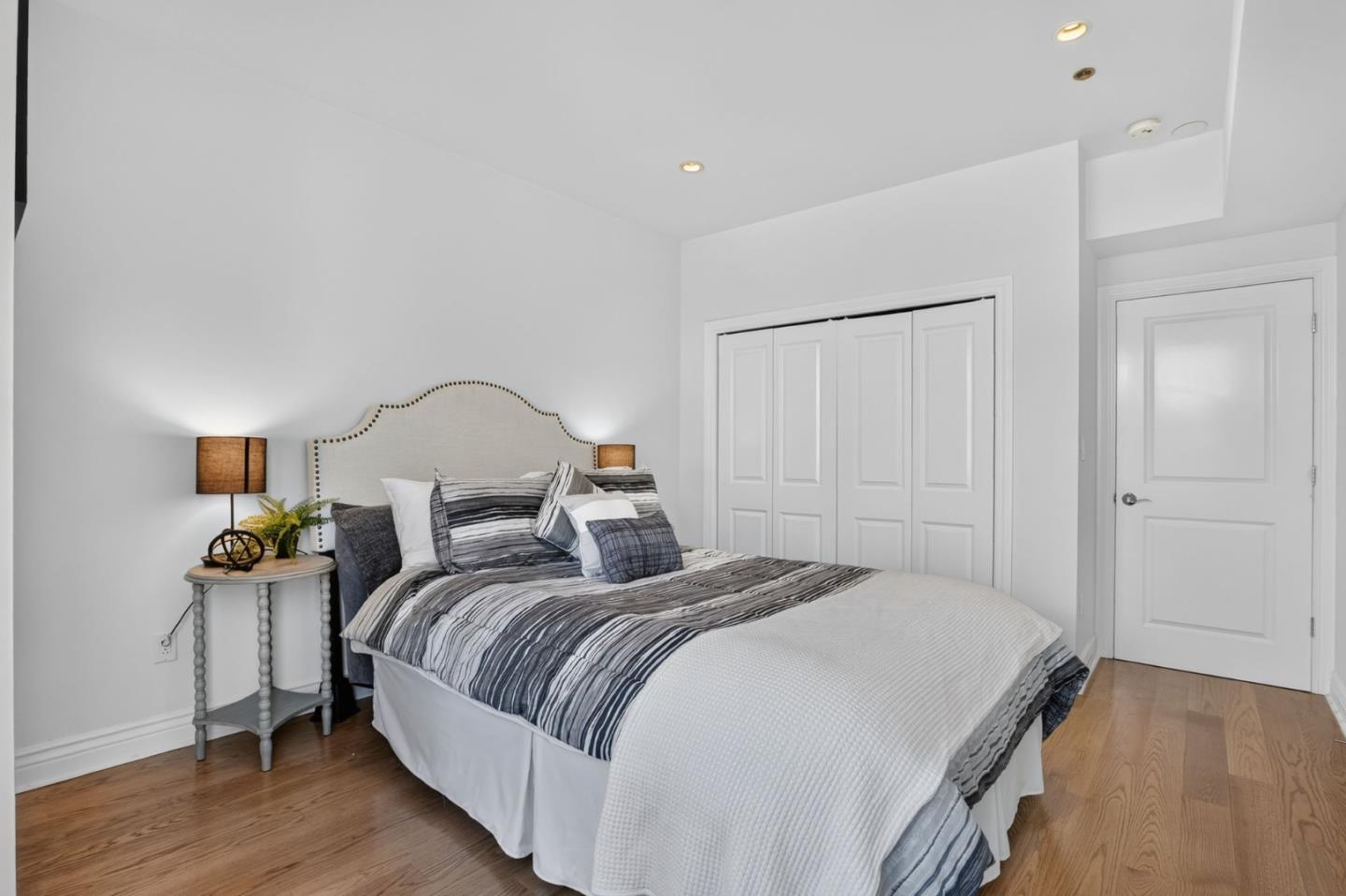 Staged bedroom with a striped bed, tufted headboard, white closet doors, and hardwood floors.