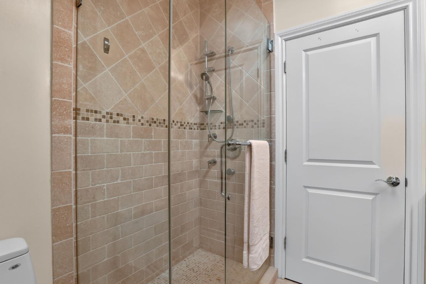 Bathroom with a glass-enclosed tiled shower, mosaic accent band, and towel hanging on the door.