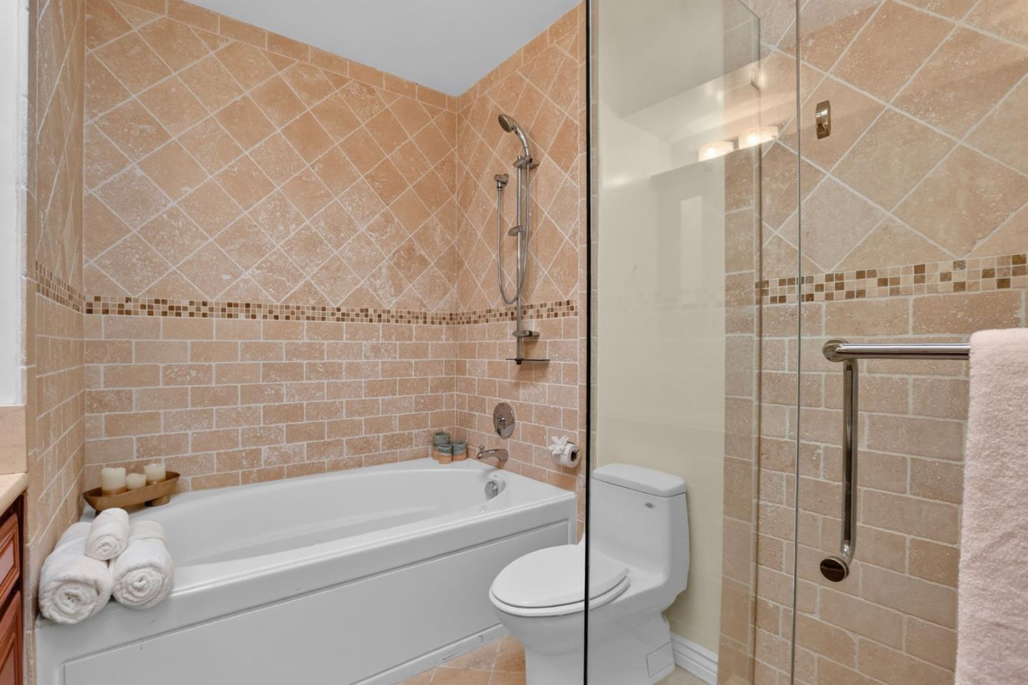 Bathroom with a white bathtub, glass shower enclosure, and beige stone tile.