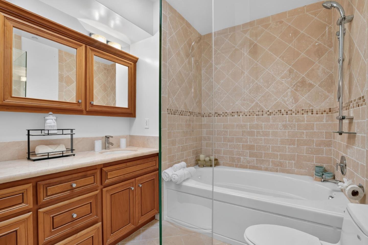 Bathroom with a glass-screened tub and shower beside a warm wood vanity.