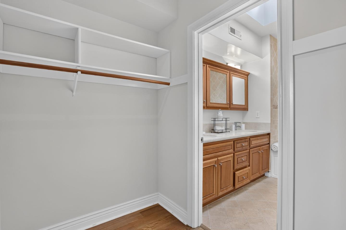 Walk-in closet beside a bathroom with warm wood vanity cabinets.